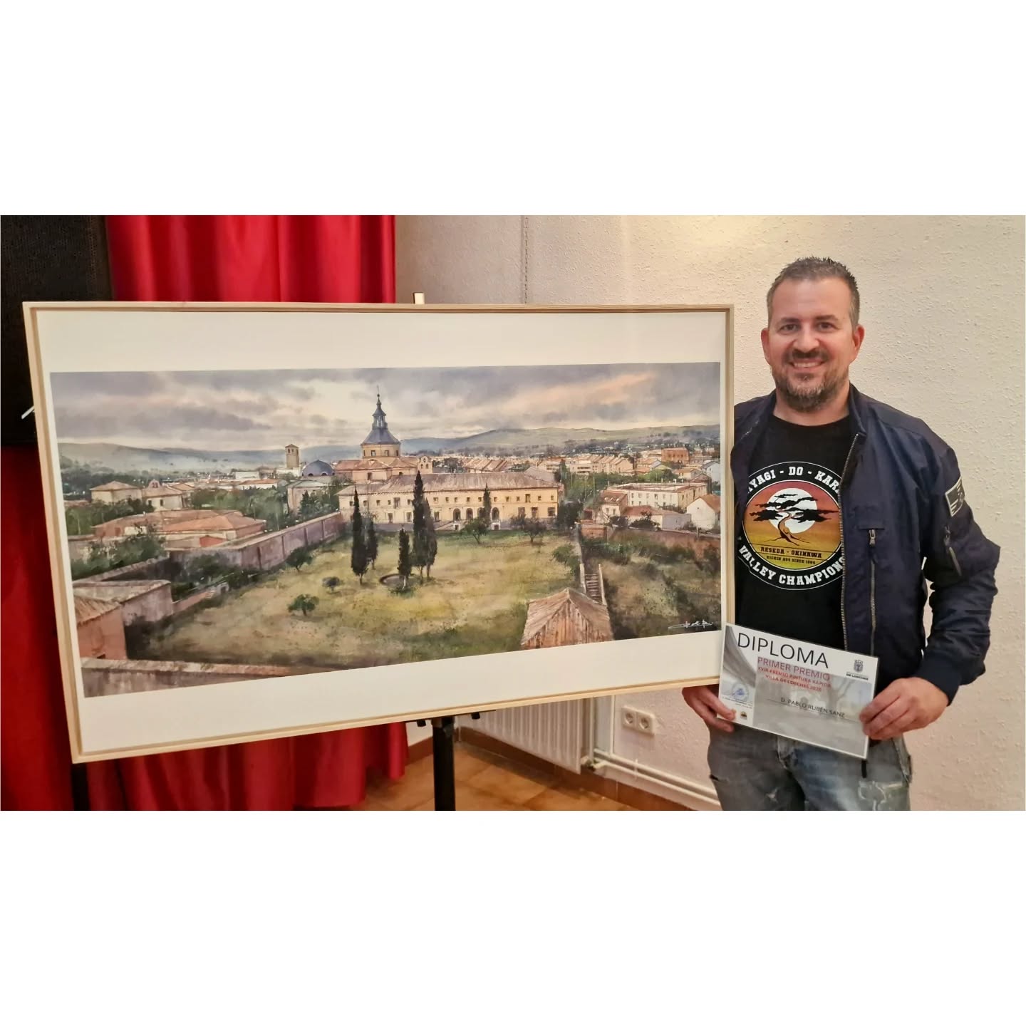 Pablo Rubén Sanz, holding a diploma next to one of his award-winning watercolors